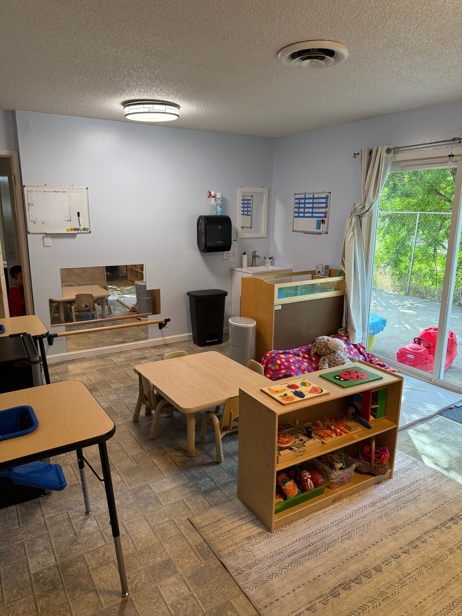 Infant and toddler classroom featuring low tables, Montessori shelves, soft lighting, and outdoor access.</p>
<p>